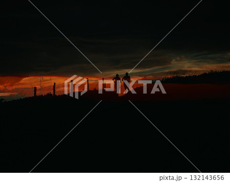 Silhouette of two runners at sunset. Two people are silhouetted against a vibrant red blue hues sunset as they run along a hill. Silhouette of two runners at sunset. Two people are silhouetted against a vibrant red blue hues sunset as they run along a hill. 132143656