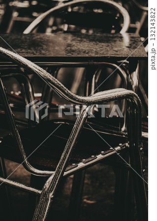 Close-up of wet metal chairs and a table in a moody, atmospheric restaurant setting. Cafe terrace after rain, creating a dark moody atmosphere Close-up of wet metal chairs and a table in a moody, atmospheric restaurant setting. Cafe terrace after rain, creating a dark moody atmosphere 132143822