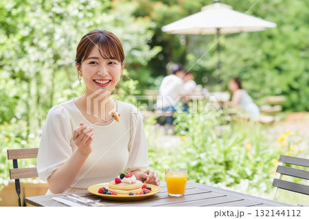 緑豊かな屋外カフェでパンケーキを笑顔で楽しむ女性の休日ブランチ 緑豊かな屋外カフェでパンケーキを笑顔で楽しむ女性の休日ブランチ 132144112