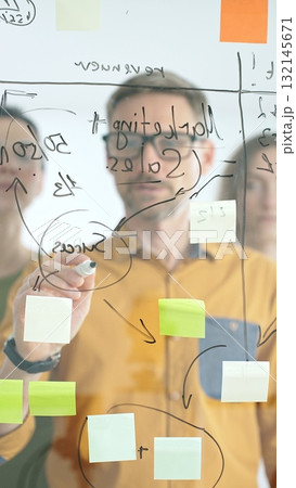 Business people team strategizing, writing collaborative notes on glass board, mapping innovative project workflow with marker in office Business people team strategizing, writing collaborative notes on glass board, mapping innovative project workflow with marker in office 132145671