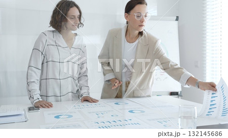 Two businesswomen are examining financial charts and statistics during a productive meeting in a modern office, demonstrating teamwork and strategic planning. Business people concept Two businesswomen are examining financial charts and statistics during a productive meeting in a modern office, demonstrating teamwork and strategic planning. Business people concept 132145686