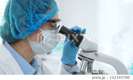 Female scientist analyzing sample through microscope, wearing protective lab gear during medical research investigation. Medicine, healthcare and science concept Female scientist analyzing sample through microscope, wearing protective lab gear during medical research investigation. Medicine, healthcare and science concept 132145700