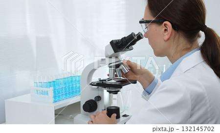 Female scientist examining microscope slide, analyzing chemical sample in sterile laboratory environment, performing precision medical research. Medicine and science concept Female scientist examining microscope slide, analyzing chemical sample in sterile laboratory environment, performing precision medical research. Medicine and science concept 132145702