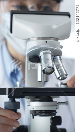 Female scientist wearing lab coat and protective glasses using a modern microscope in a laboratory setting, conducting research and experiments, close up. Health care, medicine and science concept Female scientist wearing lab coat and protective glasses using a modern microscope in a laboratory setting, conducting research and experiments, close up. Health care, medicine and science concept 132145773