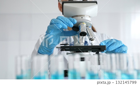 Female scientist wearing protective equipment checking microscope, analyzing blue test tubes in modern laboratory research setting. Medicine, healthcare and science concept Female scientist wearing protective equipment checking microscope, analyzing blue test tubes in modern laboratory research setting. Medicine, healthcare and science concept 132145799