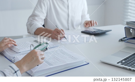Team of accountants are working together, using a magnifying glass and a calculator, to audit financial reports in office. Audit and taxes in business 132145807