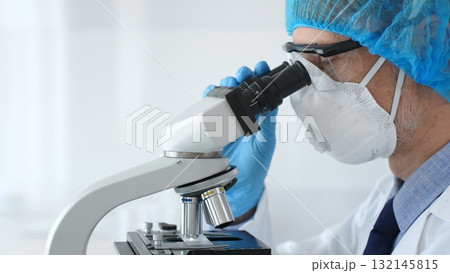 Male scientist wearing protective gear examining microscope slide, analyzing research sample in sterile laboratory environment. Health care and science concept Male scientist wearing protective gear examining microscope slide, analyzing research sample in sterile laboratory environment. Health care and science concept 132145815
