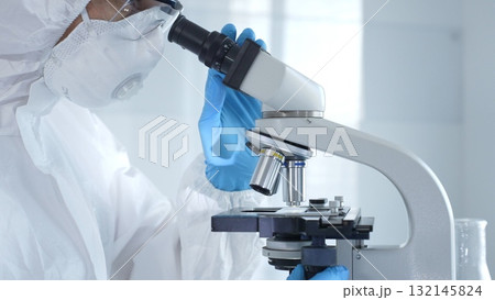 Medical virologist in a hazmat suit, mask, and gloves, diligently working at a microscope in a laboratory researching viruses. Healthcare and science concept Medical virologist in a hazmat suit, mask, and gloves, diligently working at a microscope in a laboratory researching viruses. Healthcare and science concept 132145824
