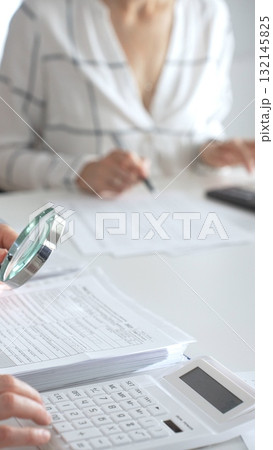 Team of accountants are working together, using a magnifying glass and a calculator, to audit financial reports in office. Audit and taxes concept Team of accountants are working together, using a magnifying glass and a calculator, to audit financial reports in office. Audit and taxes concept 132145825