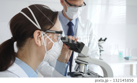 Two scientists, a man and a woman, in lab coats and protective gear, conduct research in a sterile laboratory. Concept of medicine and science 132145850