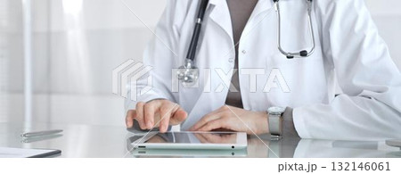 Physician in lab coat with stethoscope reviewing patient data on a tablet in a bright modern clinical office via touchscreen. Medicine and health care 132146061