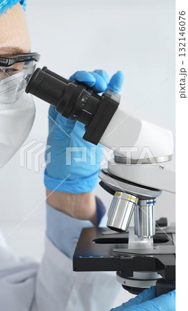 Female scientist in blue gloves and mask using microscope in laboratory setting, conducting important research and analysis, close-up. Medicine and science concept Female scientist in blue gloves and mask using microscope in laboratory setting, conducting important research and analysis, close-up. Medicine and science concept 132146076