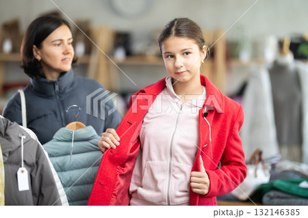 Adolescence girl try on red coat during shopping with mother in clothes store 132146385