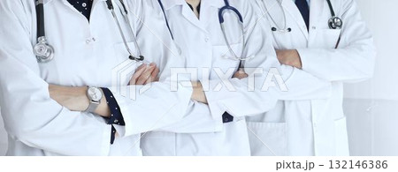 Doctors from a medical team are standing with arms crossed, wearing white coats and stethoscopes, representing unity, success, and trust in a healthcare environment 132146386