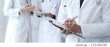 During a discussion with the medical team, a physician takes notes on a clipboard, capturing aspects of collaborative patient care, documentation, and clinical healthcare strategies During a discussion with the medical team, a physician takes notes on a clipboard, capturing aspects of collaborative patient care, documentation, and clinical healthcare strategies 132146390