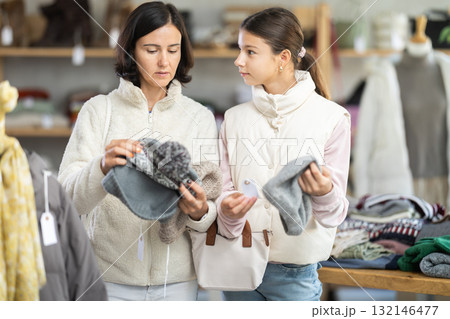 Teen girl with mother looks at products in store and selects hat. Family shopping 132146477