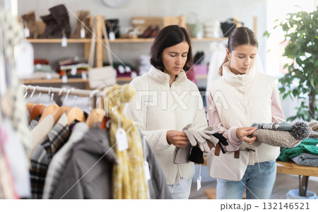 Mother and teen daughter looks at products in store and selects winter hat and gloves 132146521