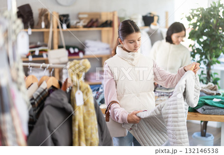 Teen girl looks at products in store and selects coat or jacket. Family shopping 132146538