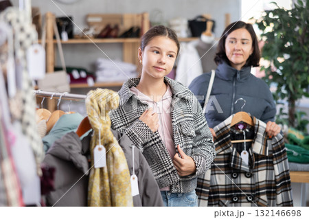 Adolescence girl try on plaid jacket during shopping with mother in clothes store Adolescence girl try on plaid jacket during shopping with mother in clothes store 132146698
