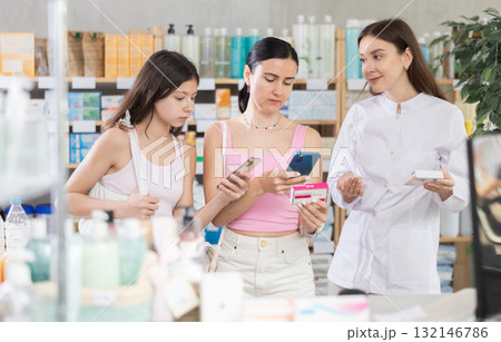 Family of mother and daughter clients choosing box of paracetamol antipyretic pills, scan QR code on label, looking at composition of medicine in drug store, young professional woman pharmacist Family of mother and daughter clients choosing box of paracetamol antipyretic pills, scan QR code on label, looking at composition of medicine in drug store, young professional woman pharmacist 132146786