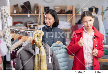 Adolescence girl try on red coat during shopping with mother in clothes store Adolescence girl try on red coat during shopping with mother in clothes store 132146788