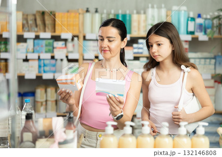 Portrait of attentive mother and daughter holding and choosing box with best pills to improve well-being in pharmacy Portrait of attentive mother and daughter holding and choosing box with best pills to improve well-being in pharmacy 132146808