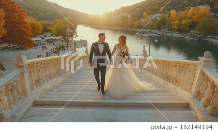 Bride and groom walking down stairs by a river at sunset. Concept of love and celebration. 132149194
