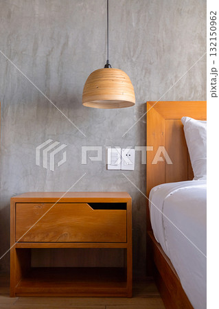 Wooden nightstand in bedroom with concrete wall and hanging lamp. 132150962