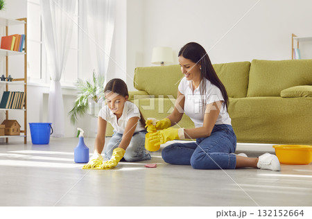 Smiling mother teaching her daughter washing the floor in the living room at home. 132152664