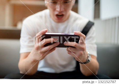 Asian man wearing glasses in white shirt is holding phone horizontally while sitting in the cafe. 132152787