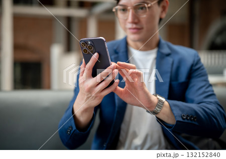 Close up of a blue suit man looking and typing on his smartphone, sitting in cafe or coffee shop. Close up of a blue suit man looking and typing on his smartphone, sitting in cafe or coffee shop. 132152840