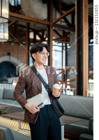 Brown suit man with glasses standing while holding a coffee cup and notebook in cafe or coffee shop. Brown suit man with glasses standing while holding a coffee cup and notebook in cafe or coffee shop. 132152855