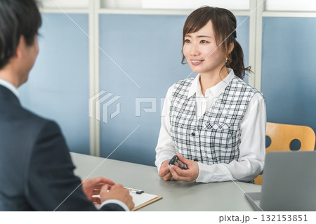 受付で車の鍵の受け渡しをする女性スタッフと顧客の男性 受付で車の鍵の受け渡しをする女性スタッフと顧客の男性 132153851