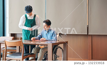 車椅子に乗った男性を接客する飲食店店員 車椅子に乗った男性を接客する飲食店店員 132153918