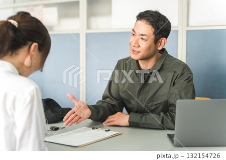 自動車整備工場の受付で説明・見積もり・提案をする整備士の男性と顧客の女性 自動車整備工場の受付で説明・見積もり・提案をする整備士の男性と顧客の女性 132154726