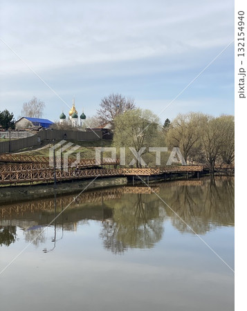 Church with golden domes reflected in calm lake surrounded by trees, wooden bridge in foreground Church with golden domes reflected in calm lake surrounded by trees, wooden bridge in foreground 132154940