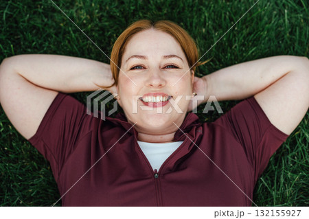 Beautiful plus size woman lying on grass after outdoors training session. 132155927