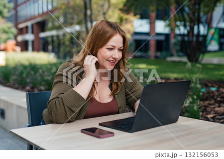 Plus size woman working on laptop outdoors. 132156053