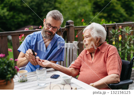 Nurse helping elderly woman measure blood sugar with glucometer. 132156125
