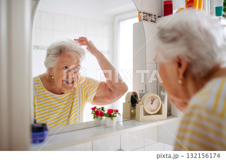 Senior woman combing her hair in bathroom. Senior woman combing her hair in bathroom. 132156174
