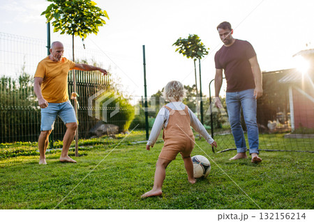 Little boy playing football with father and grandfather in backyard. Little boy playing football with father and grandfather in backyard. 132156214
