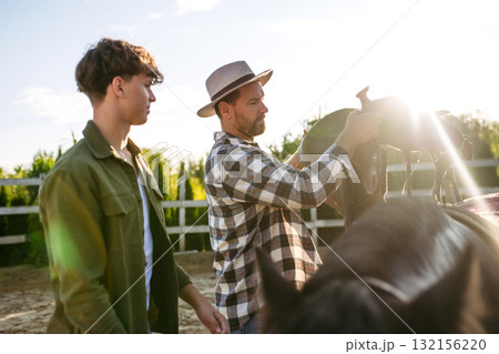 ather and son preparing horse for riding. 132156220