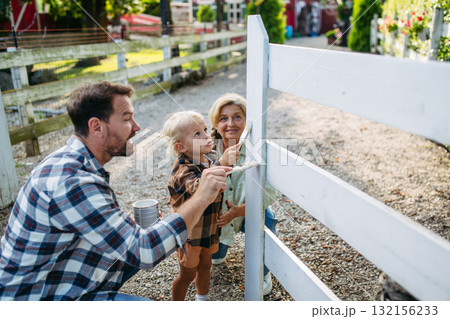 Little boy helping on farm, painting fence. 132156233