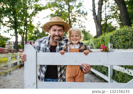 Little boy and father on farm, standing on fence. 132156235