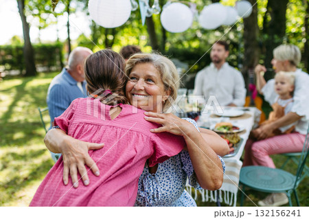 Grandmother hugging granddaughter at family garden party. 132156241