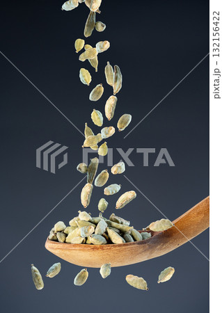Whole cardamom seeds fall from above onto a wooden spoon, ideal for aromatic seasoning and exotic recipe preparation concepts 132156422