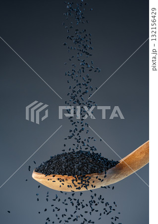 Black nigella seeds fall from above onto a wooden spoon, ideal for spice, seasoning and exotic recipe preparation concepts. Black nigella seeds fall from above onto a wooden spoon, ideal for spice, seasoning and exotic recipe preparation concepts. 132156429