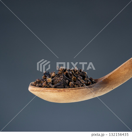 Whole dried cloves arranged on natural wooden spoon against neutral background, perfect for culinary and cooking themes 132156435