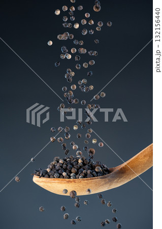 Close-up of dried black pepper corns fall from above onto a wooden spoon, perfect for gourmet food photography and spice concepts. 132156440