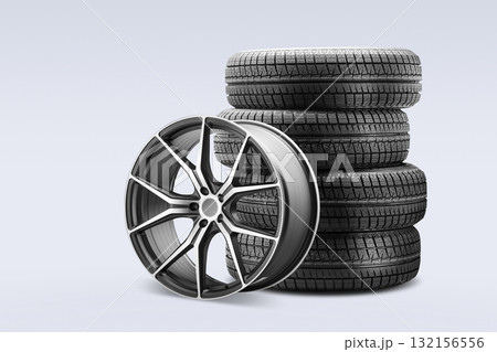 Four winter tires are stacked neatly next to a stylish alloy wheel, displaying options available for customers looking to purchase new tires at a contemporary tire store. Four winter tires are stacked neatly next to a stylish alloy wheel, displaying options available for customers looking to purchase new tires at a contemporary tire store. 132156556